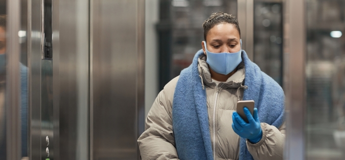 Señora abrigada dentro del ascensor con mascarilla y mirando el móvil